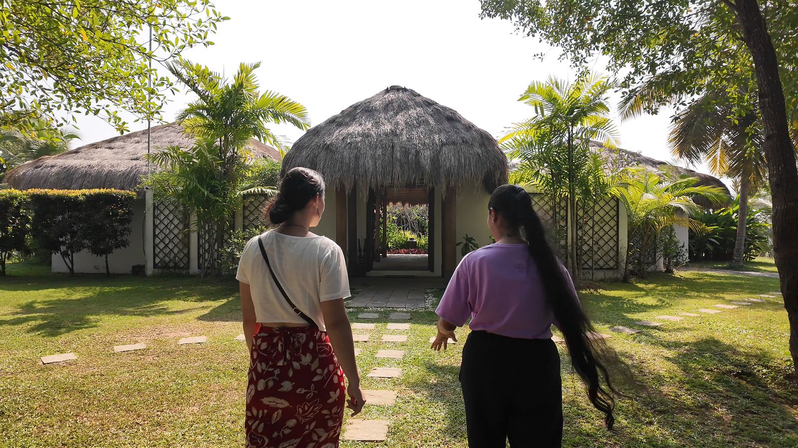 Two visitors walking toward the thatched cabanas at Tekanda Lodge